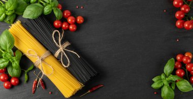 Siyah arka planda çiğ ev yapımı spagetti makarnası. Kuru siyah erişte, sarı makarna, kiraz domatesleri, yeşil fesleğen. Pişmemiş İtalyan spagetti manzarası