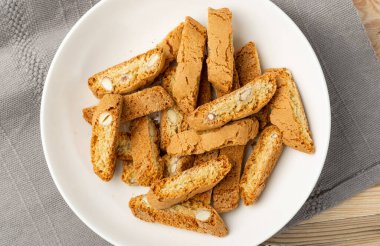 Biscotti di prato 'nun rustik masa örtüsü çuval bezi arka planı. Geleneksel İtalyan fındık kurabiyeleri. Beyaz tabakta bademli ev yapımı cantucci kurabiyesi.