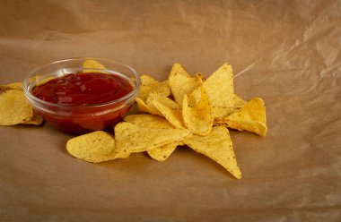 Kırsal arka planda kırmızı soslu üçgen mısır cipsi. Nacho tortilla için Meksika cipsi, mısır cipsi, mısır cipsi veya buruşuk kağıt üzerinde salsa soslu totopos.