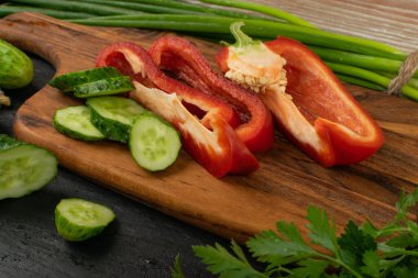 Kırsal kesim tahtasında dilimlenmiş salatalık ve yeşil sebzeli dolma biber. Taze salatalık, kırmızı biber, yeşil soğan veya taze soğan, fesleğen ve maydanoz salata için hazır.