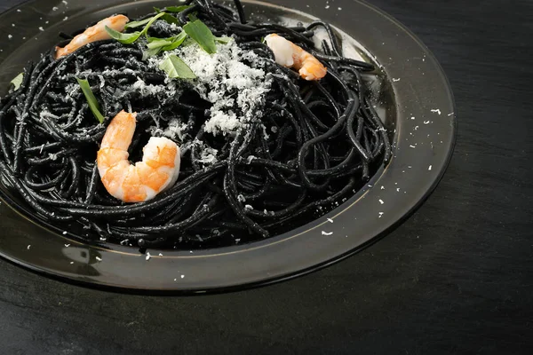 Black Italian seafood pasta with shrimps and greens on black plate. Black homemade spaghetti, noodles with cuttlefish ink, grated cheese, cooked sea food macaroni closeup