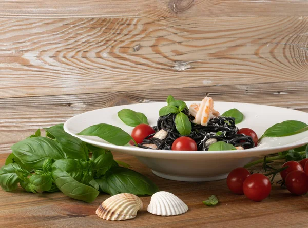 Karidesli siyah İtalyan deniz ürünleri makarnası, beyaz restoran tabağında kiraz domatesleri ve yeşillikler. Siyah ev yapımı spagetti, mürekkepbalıklı erişte, pişmiş deniz ürünleri, makarna...