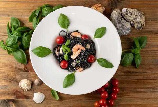 Black Italian seafood pasta with shrimps, cherry tomatoes and greens on white restaurant plate. Black homemade spaghetti, noodles with cuttlefish ink, cooked sea food macaroni top view