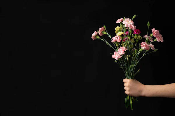 Flower bouquet in school student hand on black chalkboard background. Back to school concept, mockup with copy space