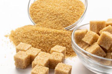 Esmer şeker küpleri ve beyaz arka planda kum. Çiğ işlenmemiş kamış şekeri yığını