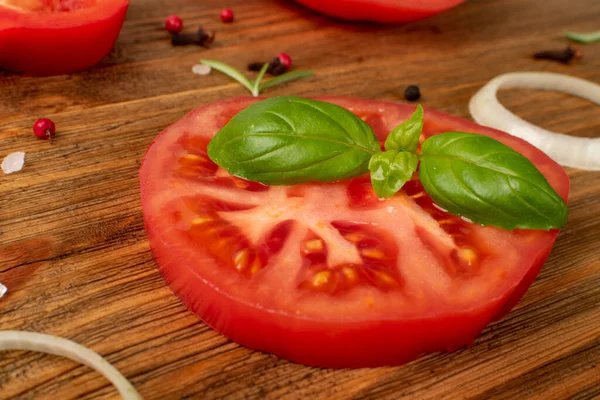 Macro photo of sliced tomatoes and basil. Big tomato slice, fresh herbs and spices on wood rustic background