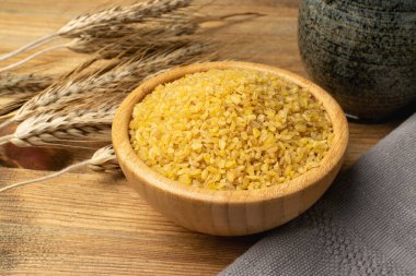 Ahşap arka planda ahşap kasede bulgur yığını. Çiğ bulguru yığını, kavrulmuş haşlanmış buğday tohumu, yakın çekim mısır gevreği.