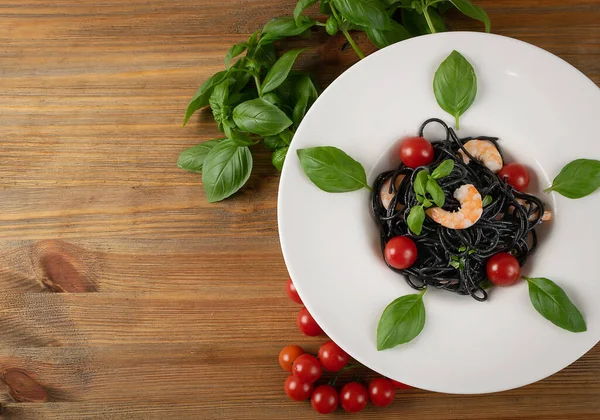 白レストランプレート上にエビ チェリートマトと緑と黒イタリアのシーフードパスタ 黒自家製スパゲティ 調理されたイカ墨マカロニコピースペーストップビュー — ストック写真