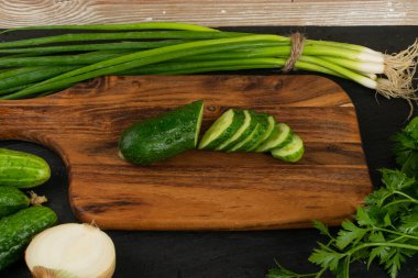 Kırsal kesim tahtasında yeşil sebzeli dilimlenmiş salatalık. Taze salatalık, yeşil soğan ya da taze soğan, fesleğen ve maydanoz salata için hazır.