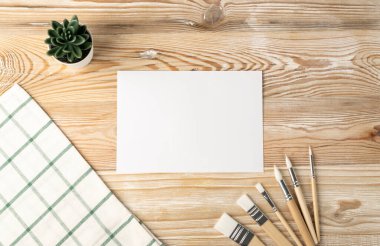 Ahşap masa üzerinde fırçaları ve manzarası olan asgari sanatçı modeli. Beyaz kağıt arkaplan oluşturur, kopyalama alanı ile resim çerçevesi