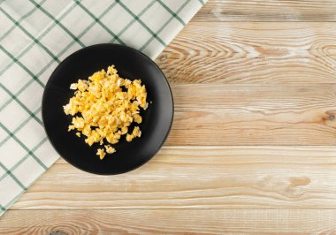 Çırpılmış yumurta ya da siyah tabakta omlet ve fotokopi alanı olan ahşap masa üstü manzarası. Kontrol edilmiş masa örtüsü ve omletli kırsal mutfak modeli.