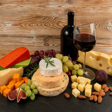 Peynir tabağı çeşitliliği, sarı, beyaz ve mavi gorgonzola tabağı kırmızı şarap bardağı, peynir tahtası, çeşitli doğranmış süt ürünleri, ahşap üzerinde kokulu Fransız peyniri.