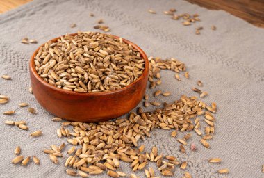 Süt devedikeni tohumu yığını, silybum marianum taneleri, kuru mübarek süt devedikeni meyveleri, gri arka planda devedikeni çekirdekleri, ahşap kase, doğal organik şifalı bitkiler.