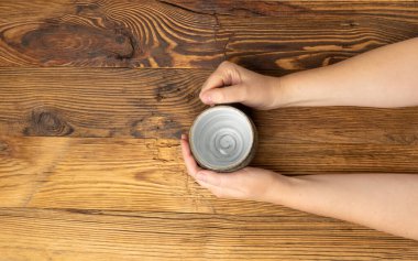 Hand Holds Kupası, Elde Boş Kupa, Kahve Kupası, Çay Fincanı, Sıcak İçecek Mockup, Tahta Masada Kollar Altında Gri Kupa, Metin Üst Görünümü için Kopya Alanı olan Rustik Arkaplan