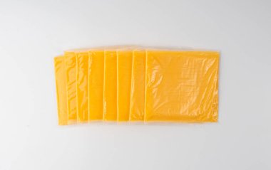 Amerikan peyniri izole edilmiş, işlenmiş peynir dilimi, ince sarı çedar peyniri, beyaz arka planda tost ve sandviç için plastik bir pakete sarılmış.