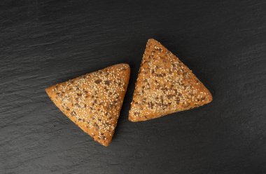Üçgen çörekler yakın plan. Susamlı ve keten tohumlu buğday ekmeği, siyah arka planda sağlıklı tahıl fırını.