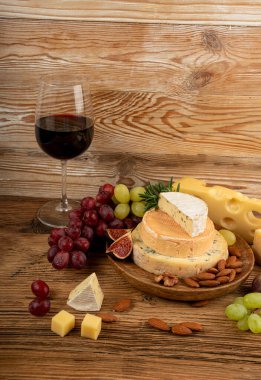 Peynir tabağı çeşitliliği, sarı, beyaz ve mavi gorgonzola tabağı kırmızı şarap bardağı, peynir tahtası, çeşitli doğranmış süt ürünleri, ahşap üzerinde kokulu Fransız peyniri.