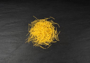 Çiğ vermicelli, altın çorbalı makarna yuvarlak makarna, küçük dağınık ev yapımı erişte, ince makarna, İtalyan filini makarna siyah taş arka plan manzaralı.