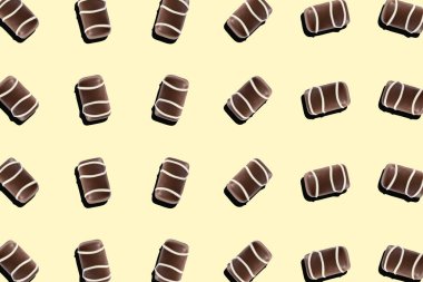 Sarı arka planda dekoratif çizgileri olan çeşitli çikolatalı pralinaların üst görüntüsü. Bireysel kahverengi şekerler eğlenceli bir tekrarlama kalıbı oluşturur
