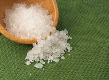 Ölü deniz tuzu yığını, vücut spa 'sı için beyaz kristaller, ezilmiş buza benzer sodyum klorür, ahşap kasedeki spa fırçası.