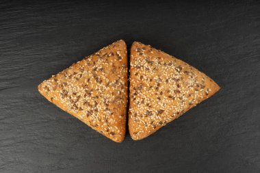 Üçgen çörekler yakın plan. Susamlı ve keten tohumlu buğday ekmeği, siyah arka planda sağlıklı tahıl fırını.