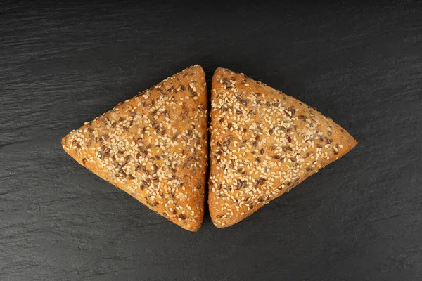 Üçgen çörekler yakın plan. Susamlı ve keten tohumlu buğday ekmeği, siyah arka planda sağlıklı tahıl fırını.
