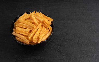 Kızarmış cips çubukları siyah kasede, parmak patates cipsi, altın ayakkabı teli patates kızartması, patates kızartması, kızarmış patates, koyu taş masa arkasında patates kızartması.