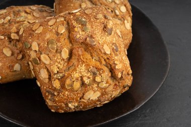 Kabak çekirdeği ekmeği yakın, makro kahvaltı ruloları ve pepita tohumları. Fitness karesi çöreği, sağlıklı burger, kabak tohumlu çörek ve siyah arka plan.