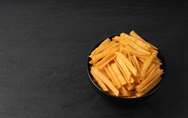 Kızarmış cips çubukları siyah kasede, parmak patates cipsi, altın ayakkabı teli patates kızartması, patates kızartması, kızarmış patates, koyu taş masa arkasında patates kızartması.