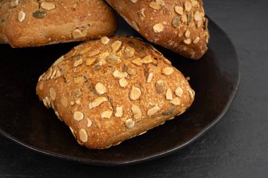 Kabak çekirdeği ekmeği yakın, makro kahvaltı ruloları ve pepita tohumları. Fitness karesi çöreği, sağlıklı burger, kabak tohumlu çörek ve siyah arka plan.