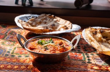 Tereyağlı paneer masala, peynirli Hint körisi peynir kübü, baharatlı tavuk korması, domates kremi soslu geleneksel yemek, geleneksel tekstil kaplı masa üzerindeki metal tabak.