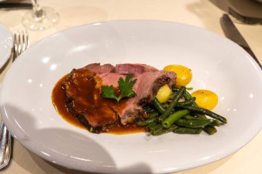 Yeşil kuşkonmaz fasulyeli biftek ve restoran tabağında kahverengi soslu patates, bulanık arka plan.