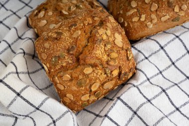 Kabak çekirdeği ekmeği yakın, makro kahvaltı ruloları ve pepita tohumları. Spor salonu çöreği, sağlıklı hamburger, kabak tohumlu çörek ve kırsal masa örtüsü.