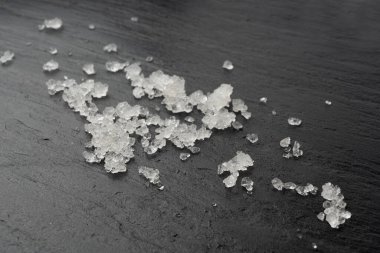 Ölü deniz tuzu yığını, vücut spa 'sı için dağınık beyaz kristaller, ezilmiş buza benzer sodyum klorür, siyah arka planda spa fırçası.