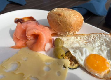 Otel restoranında her şeyi kapsayan tipik bir kahvaltı. Yağda yumurta, peynir, zeytinli füme somon ve bir dilim patlıcan.