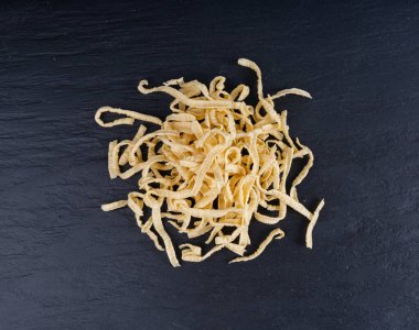 Passatelli spatzle makarna yığını, çiğ spaetzle noodle, ev yapımı Alman makarnası, siyah masa arkasında samanlı spaetzle yumurtası makarna.