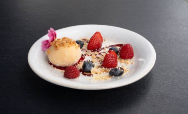 Meyveli mochi pirinç keki, beyaz daifuku, Japon geleneksel tatlısı, kremalı ve anko dolgulu yuvarlak wagashi, çilekli Asya şekeri, yaban mersini ve siyah arka planda çiçek.