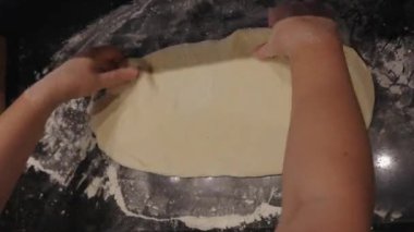 Pizza hamurunu un masa arkasına seriyorum. Kadın elleri ekmek hamurunu koyu bulanık arka plana sarar