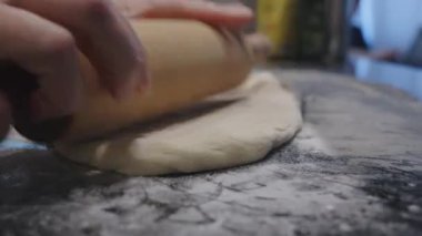 Pizza hamurunu un masa arkasına seriyorum. Kadın elleri ekmek hamurunu koyu bulanık arka plana sarar