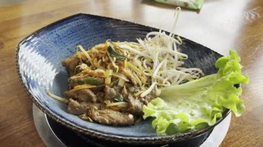 Fındıklar Pad Thai ya da Phad tha Asya eriştelerinin üzerine düşüyor. Çin pirinçli makarna, etli Tayland yemeği, erişte, taze lahana salatası ve bulanık arka planda sokak restoranında yeşillikler.