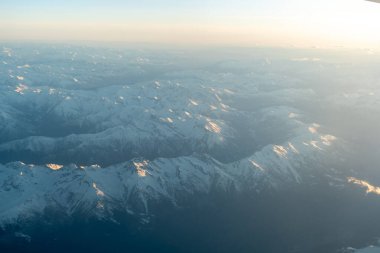 Gün batımında yukarıdan görünen karla kaplı dağ zirveleri Alp manzarasının tepelerini ve vadilerini aydınlatan yumuşak altın ışıkla