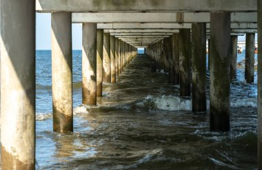Concrete pier piles receding into perspective over water. View from below on thick vertical supports submerged in sea or lake, with strong geometric lines