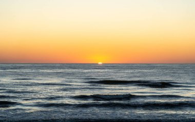 Güneşin yarısı deniz ufkunun altında gizlenirken, portakal rengi gradyan zıt sularla denizin üzerinde güzel bir günbatımı.