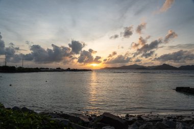 La Digue 'den gün batımı manzarası Praslin Adası' nın silueti ve sakin denizde altın yansıması