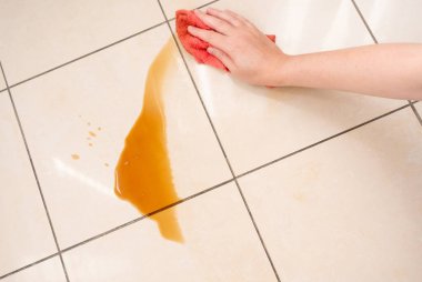 Dökülmüş kahve, kadın fayanslı zemindeki kahve lekesini siliyor, dökülen fincanla karışık sızıntı, dökülen kahverengi içki temizliği.