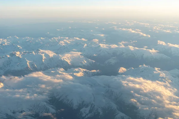 Gün batımında yukarıdan görünen karla kaplı dağ zirveleri Alp manzarasının tepelerini ve vadilerini aydınlatan yumuşak altın ışıkla