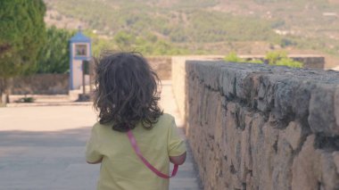 Küçük bir çocuk taş bir duvar boyunca dini bir tapınağa doğru yürüyor, antik kalıntıları keşfetmek için yaz tatili gününün tadını çıkarıyor.