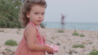 Sevimli çocuk fotoğrafçılığı keşfediyor, plaj anılarını pembe bir oyuncak kamerayla yakalıyor.