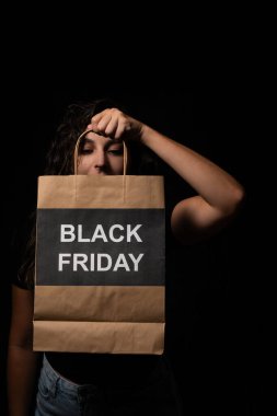 Stüdyoda, elinde siyah bir Cuma alışveriş torbası tutan genç bir kadının fotoğrafı.