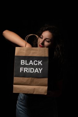 Müşteri, içinde kara Cuma yazıları olan alışveriş çantasına bakıyor. Büyük satışlar ve indirimlerin keyfini çıkarıyor.